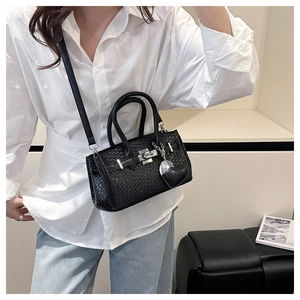 Detail of black woven Kelly bag with silver hardware and heart pendant on model
