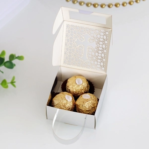 Macro view of white laser-cut wedding favor box with hollow cross and gold chocolates