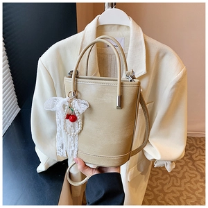 Détail du sac seau beige en cuir PU avec pendentif cerise et nœud en dentelle