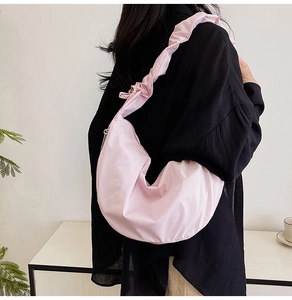 Detail of light pink crescent dumpling bag with ruffled shoulder strap worn by model