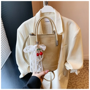 Détail du sac seau beige avec perles cerise et pendentif nœud en dentelle blanche
