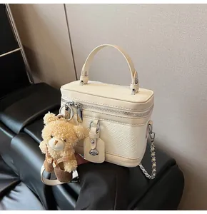 Détail du sac seau tressé crème avec bandoulière chaîne et pendentif ours mignon