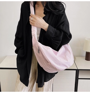 Detail of light pink crescent dumpling bag worn by model with metallic zipper closure