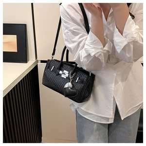 Detail of black woven Kelly bag with silver lock and heart charm on white shirt