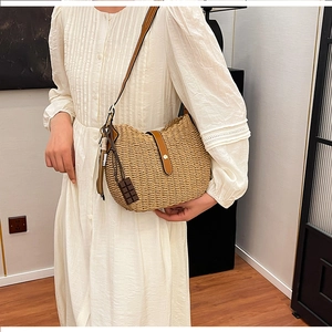 Detail of woven straw shoulder bag with brown leather strap and chocolate charm