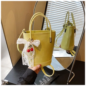 Détail d'un sac seau jaune pâle avec nœud en dentelle, perles et breloques cerise
