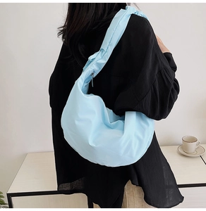 Side view of a light blue pleated dumpling bag worn over a black jacket on shoulder