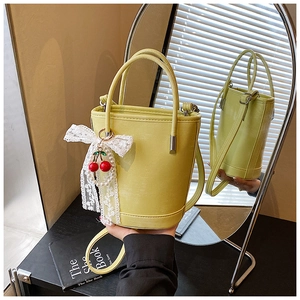 Détail du sac seau en cuir vert jaune avec breloque cerise rouge et nœud en dentelle blanche