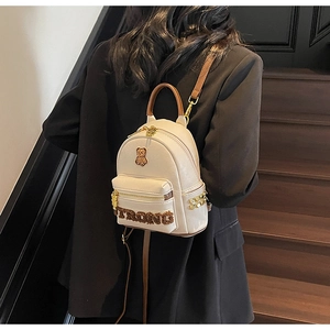 Détail du sac à dos en PU crème avec logo ours doré et lettrage TRONG en peluche