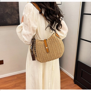 Close-up of woven straw shoulder bag with brown leather strap worn by a model