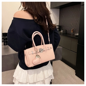 Detail of pink woven texture crossbody bag with heart pendant and metal clasp