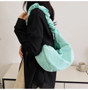 Detail of mint green crescent bag with ruffled shoulder strap worn by a female model