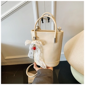 Détail d'un sac seau crème avec nœud en dentelle, breloques cerises et perles en cuir PU