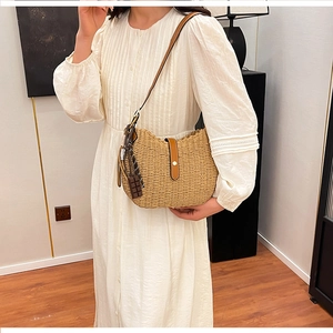 Detail of handwoven crescent straw shoulder bag with leather strap on a cream dress
