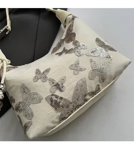 Close-up of beige fabric shoulder bag with sparkling silver sequin butterfly embroidery