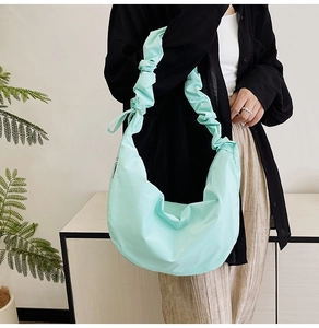 Detail of mint green pleated shoulder bag featuring a decorative bow on the strap