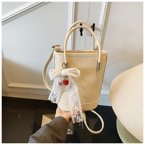 Détail d'un sac seau beige avec nœud en dentelle blanche et breloques cerise et perle