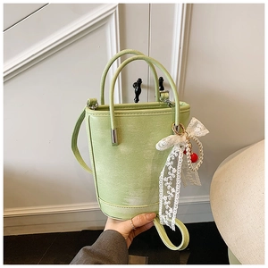 Détail du sac seau vert en cuir avec nœud en dentelle blanche et breloque cerise perle