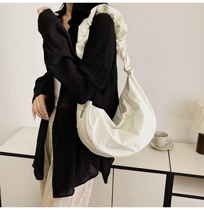 Detail of creamy pleated crescent bag featuring ruffle shoulder strap and silver zipper