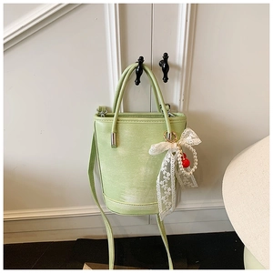 Détail du sac seau vert clair avec nœud en dentelle, perles et breloques cerise