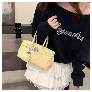 Detail of light yellow woven texture handbag with silver lock and heart charm accessory
