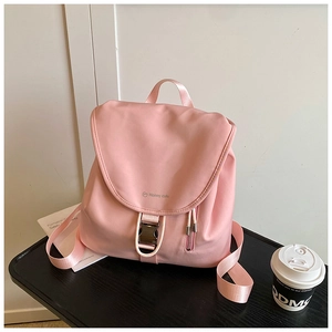 Dettaglio zaino in nylon rosa con patta e fibbia metallica su superficie di legno