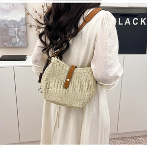 Detail of woven straw bucket bag with brown leather strap worn by a model in interior