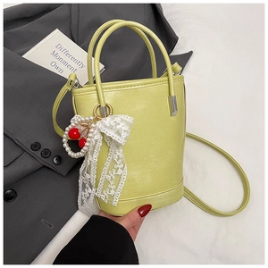 Détail du sac seau vert clair avec pendentif cerise en perles et nœud en dentelle