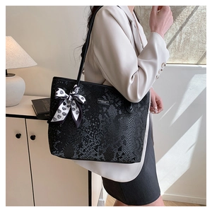 Detail of snake skin texture black tote bag with white heart scarf on shoulder strap