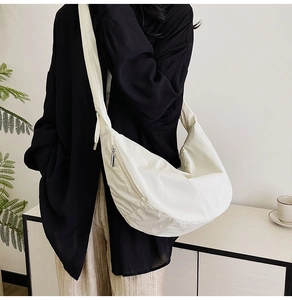 Side view of beige nylon dumpling bag with wide shoulder strap worn by a model