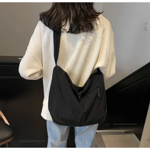Dettaglio di una grande borsa a tracolla in nylon nero con ampia cinghia indossata dal modello
