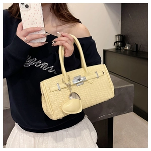 Close-up of a yellow woven Kelly handbag with silver hardware and a heart charm