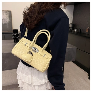 Detail of yellow woven texture Kelly bag with metallic lock and heart charm