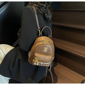 Détail du sac à dos en PU marron avec écusson d'ours en 3D et fermetures éclair dorées