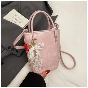 Détail d'un sac seau rose en cuir lavé avec pendentif cerise et nœud de perles en dentelle