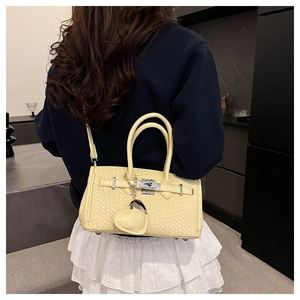 Close-up of yellow woven texture leather handbag with metal turn-lock and heart charm