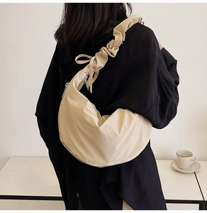 Detail of beige nylon crescent bag featuring pleated shoulder strap and silver metal zipper