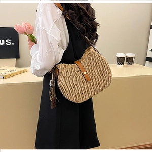 Detail of straw woven bucket bag with brown leather strap and decorative tassels