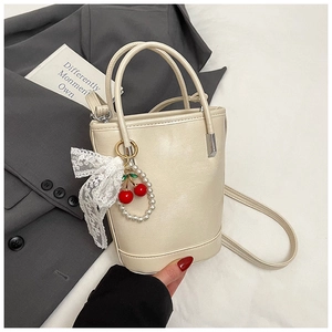 Détail du sac seau crème avec pendentif cerise et perle et nœud en dentelle blanche