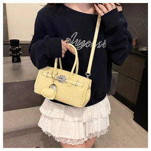 Close-up of woven texture light yellow handbag with silver twist lock and heart pendant