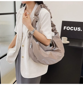 Detail of a large light brown pleated crescent bag with wide shoulder strap on a model