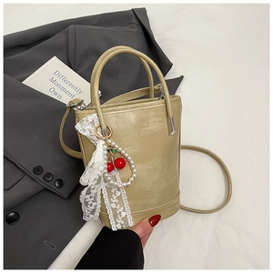 Détail du sac seau beige avec nœud en dentelle et pendentif cerise et perles