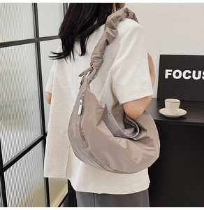 Detail of taupe crescent nylon shoulder bag featuring stylish ruched strap on model