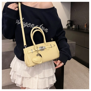 Detail of light yellow woven Kelly bag with metal twist lock and heart charm accessory