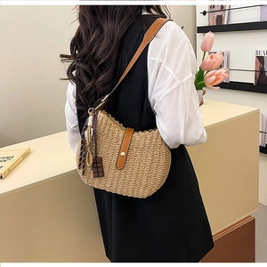 Detail view of woven straw bucket bag with brown leather strap and chocolate charm