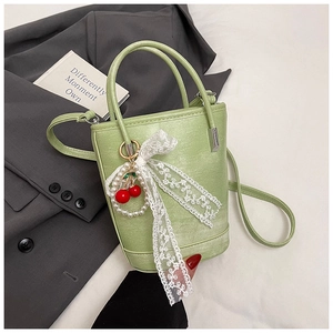 Détail du sac seau vert clair avec nœud en dentelle et breloque cerise sur veste