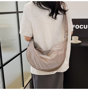Rear view of a model wearing a beige pleated crescent crossbody bag in a city cafe