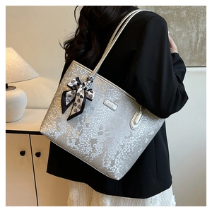 Detail view of silver snakeskin tote bag with bow charm showing texture and shoulder straps