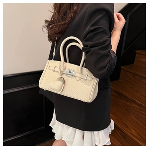 Detail of a beige woven textured handbag with silver twist lock and heart charm