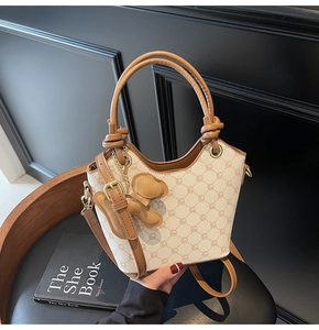 Détail du sac seau en toile avec finitions en cuir marron, bijoux dorés et charm ours